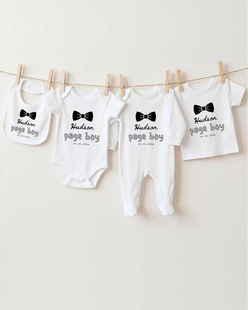 A row of four white baby clothes with black text and bow ties, hanging on a clothesline.