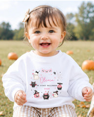 A smiling baby girl wearing a white sweater with a personalized design and text.