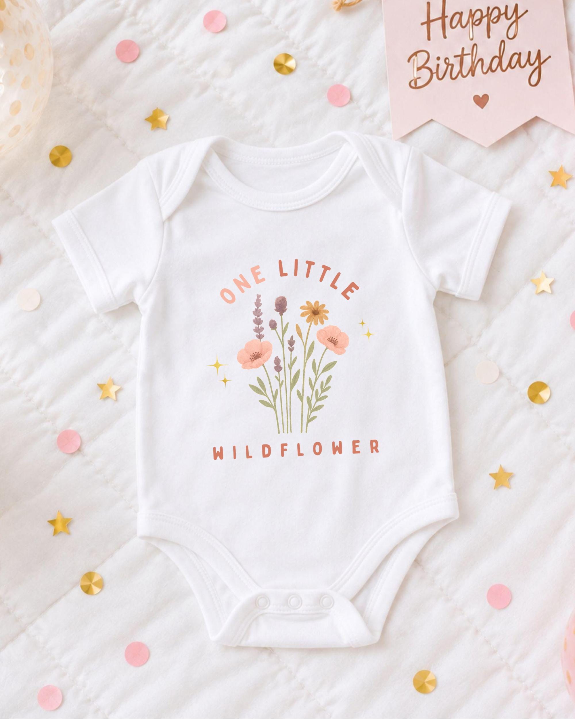 A white onesie with a floral design and the text "One Little Wildflower" printed on it, surrounded by confetti and a birthday card.