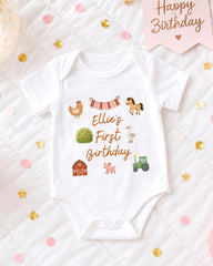 A white baby onesie with a personalized birthday message printed on it, surrounded by confetti and a birthday card.