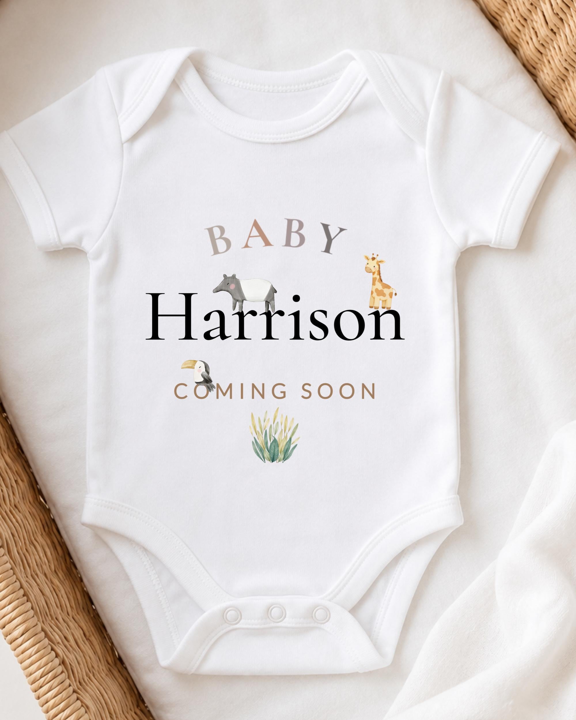 A white baby onesie with the text "BABY Harrison COMING SOON" printed on it, along with illustrations of a giraffe and a bird.