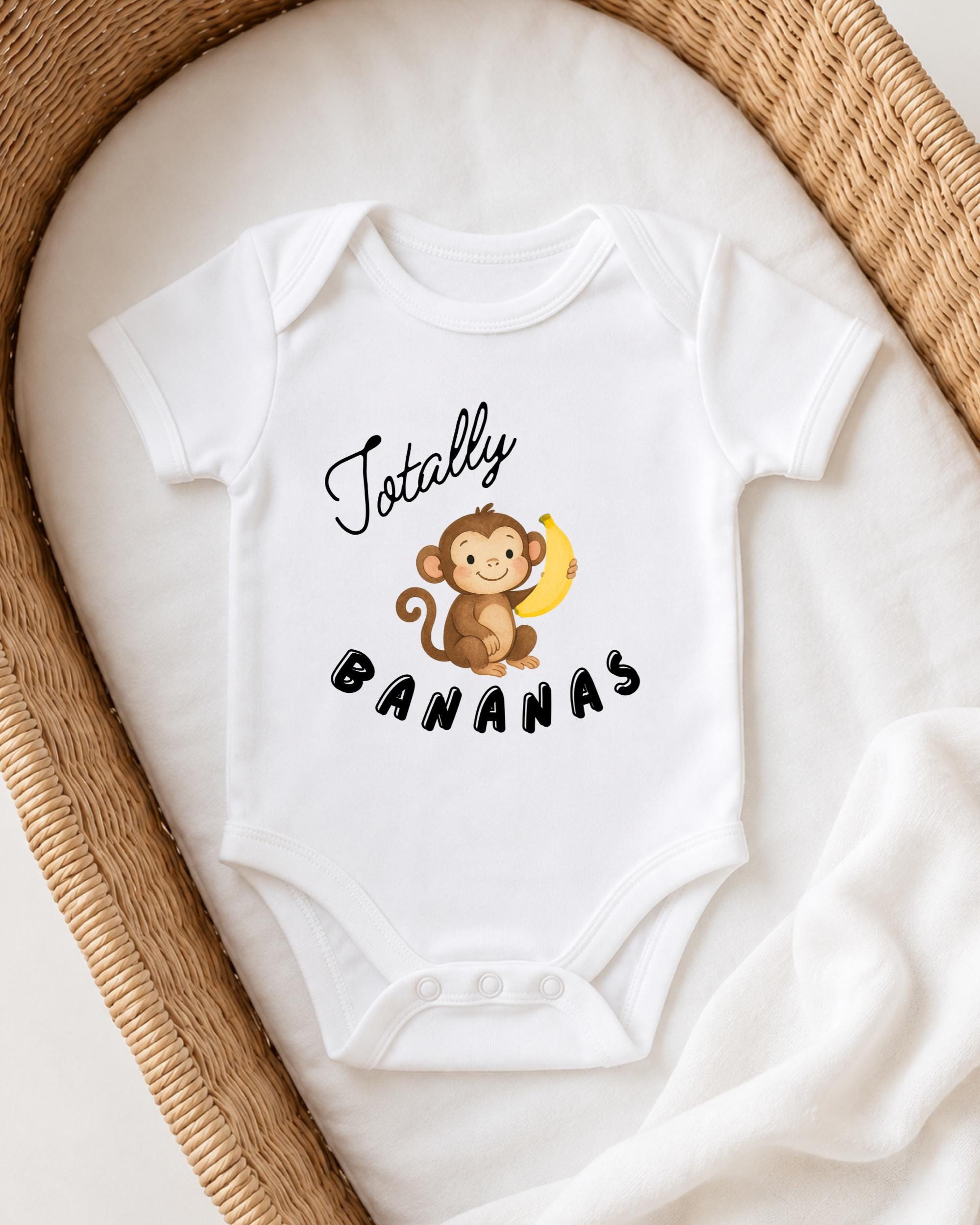 A white onesie with a cartoon monkey and the text "Totally Bananas" printed on it, laid out on a white blanket.