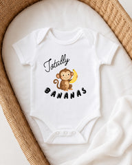 A white onesie with a cartoon monkey and the text "Totally Bananas" printed on it, laid out on a white blanket.