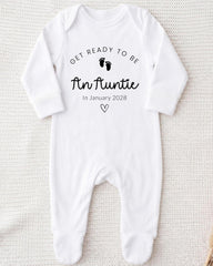A white onesie with the text "Get ready to be An Auntie" printed on it, along with a heart symbol and the date "In January 2028".