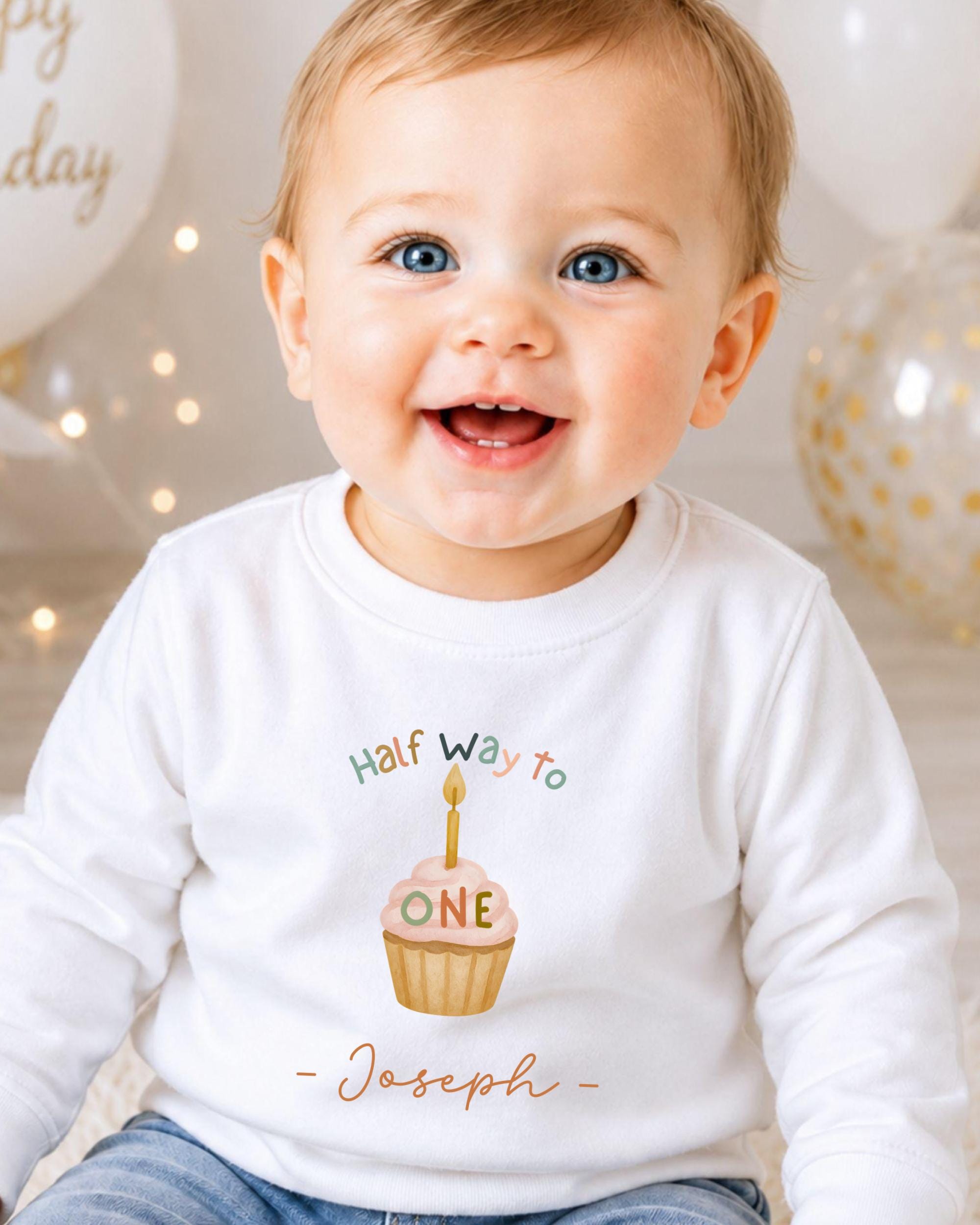 A smiling baby boy wearing a white shirt with a birthday cake design and the text "Half Way To Joseph" printed on it.