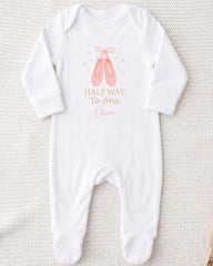 A white onesie with a graphic of ballet slippers and the text "Half way to one - Olivia" printed on it.