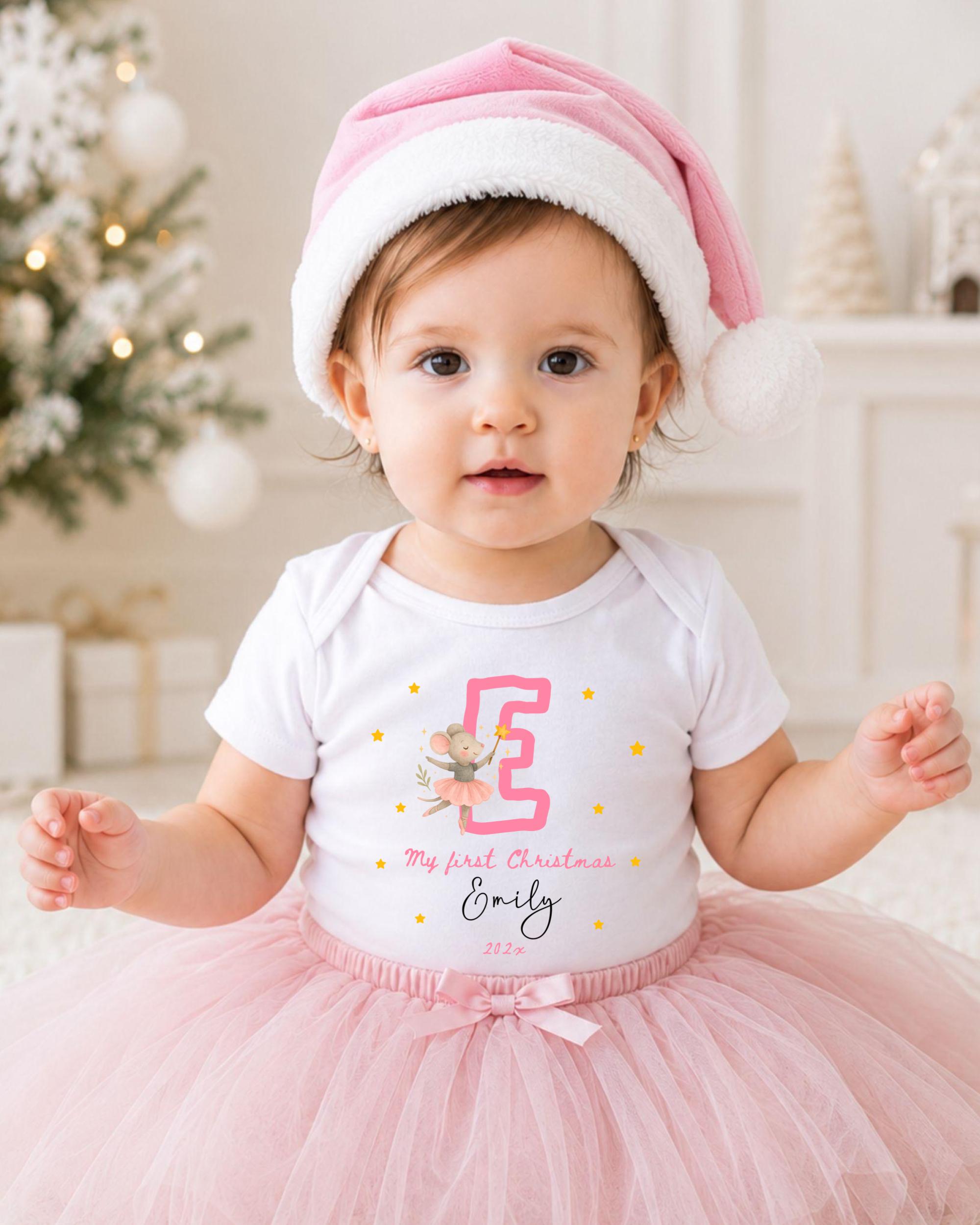 A young girl wearing a pink tutu and a pink Santa hat, with a white t-shirt featuring a pink letter and a small illustration of a mouse.