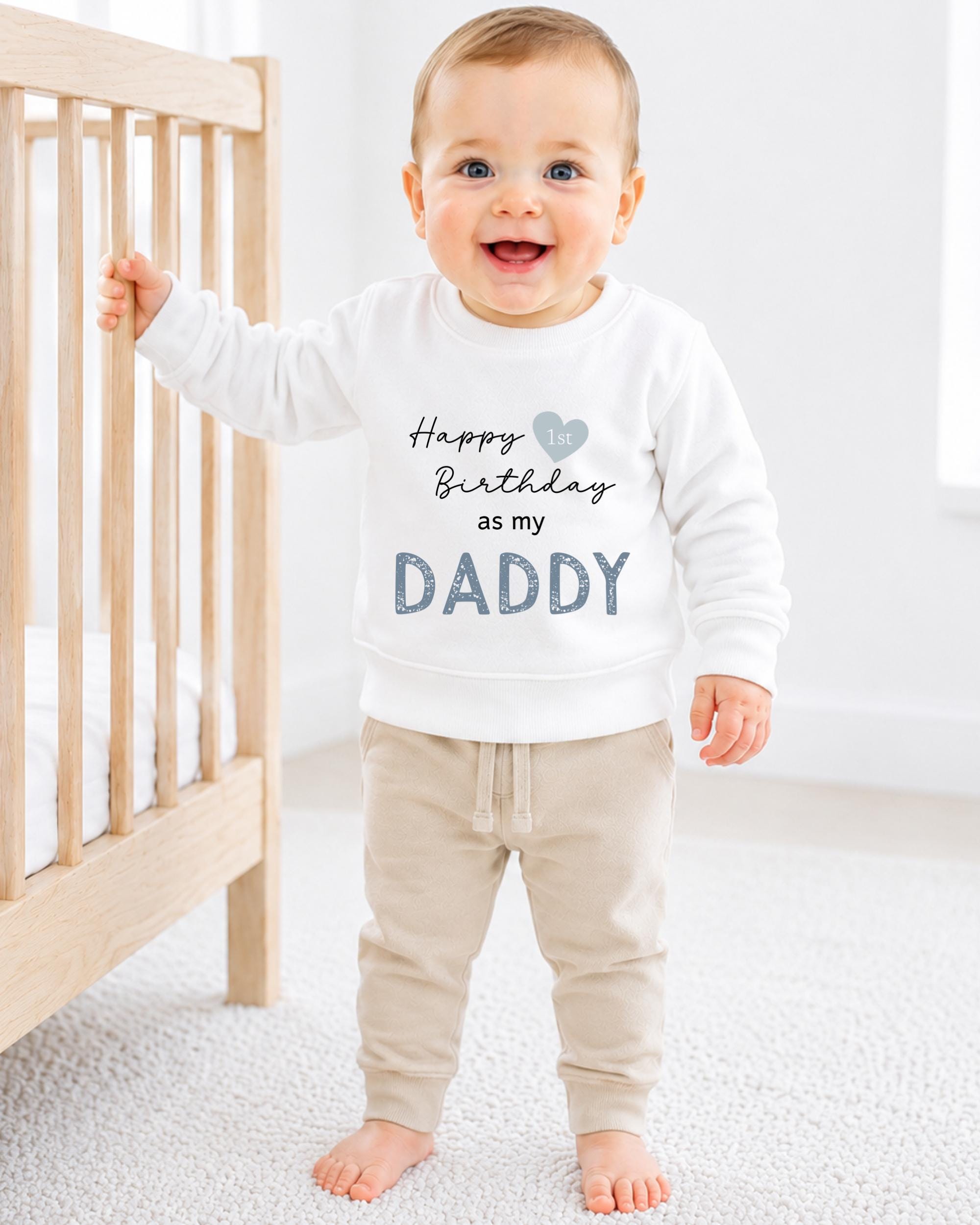 A smiling baby boy wearing a white sweatshirt with the text "Happy 1st Birthday as my Daddy" printed on it.