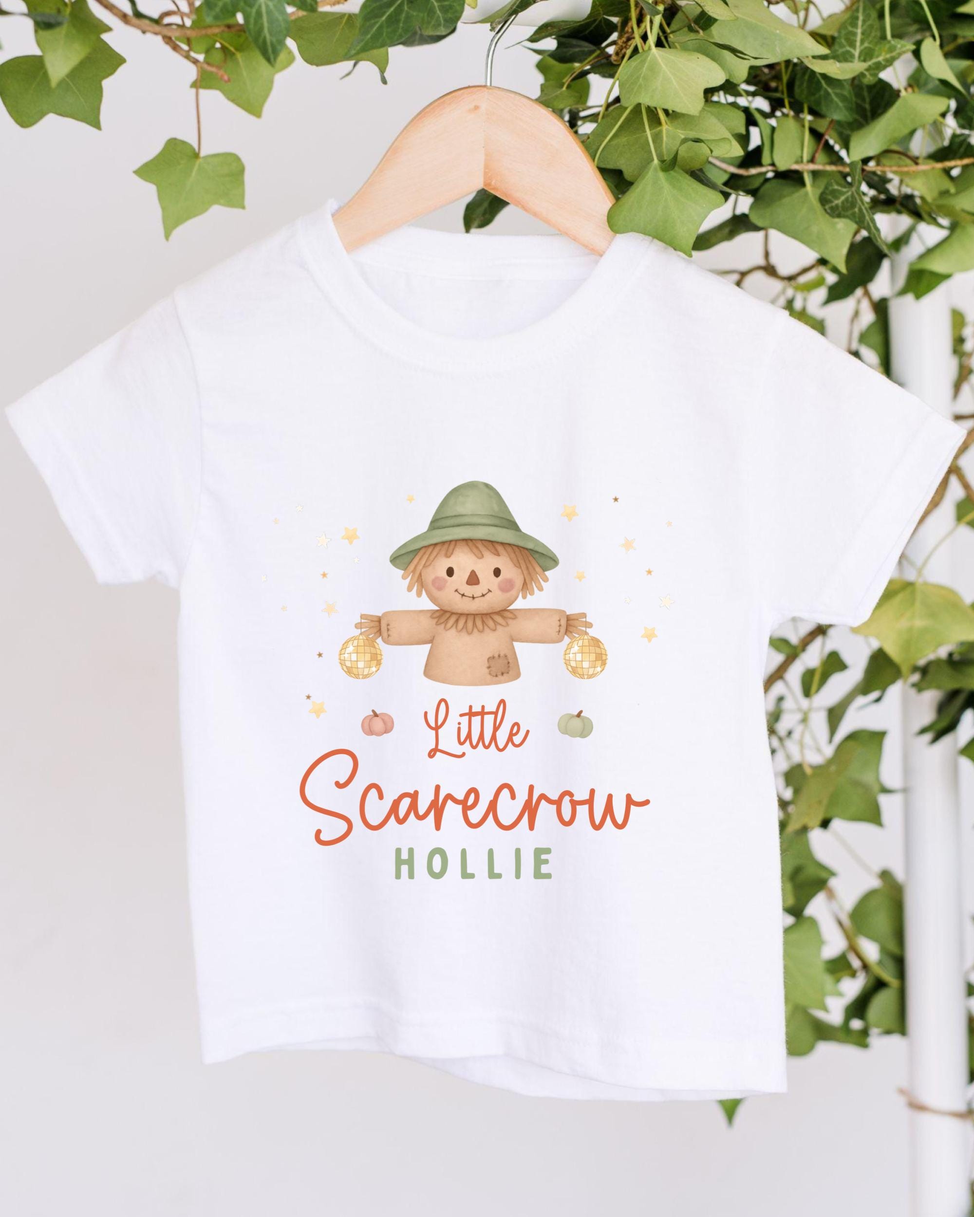 A white t-shirt with a cartoon scarecrow design and the text "Little Scarecrow Hollie" printed on it.