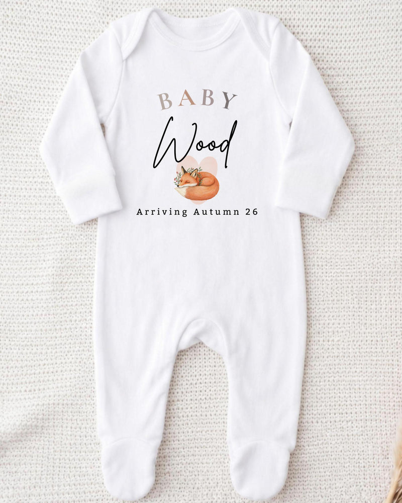 Personalisable white Baby Grow with beige 'BABY', black script 'Wood', a sleeping orange fox and 'Arriving Autumn 26' lettering.