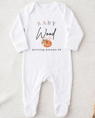 A white onesie with the text "BABY WOOD Arriving Autumn 26" printed on it.