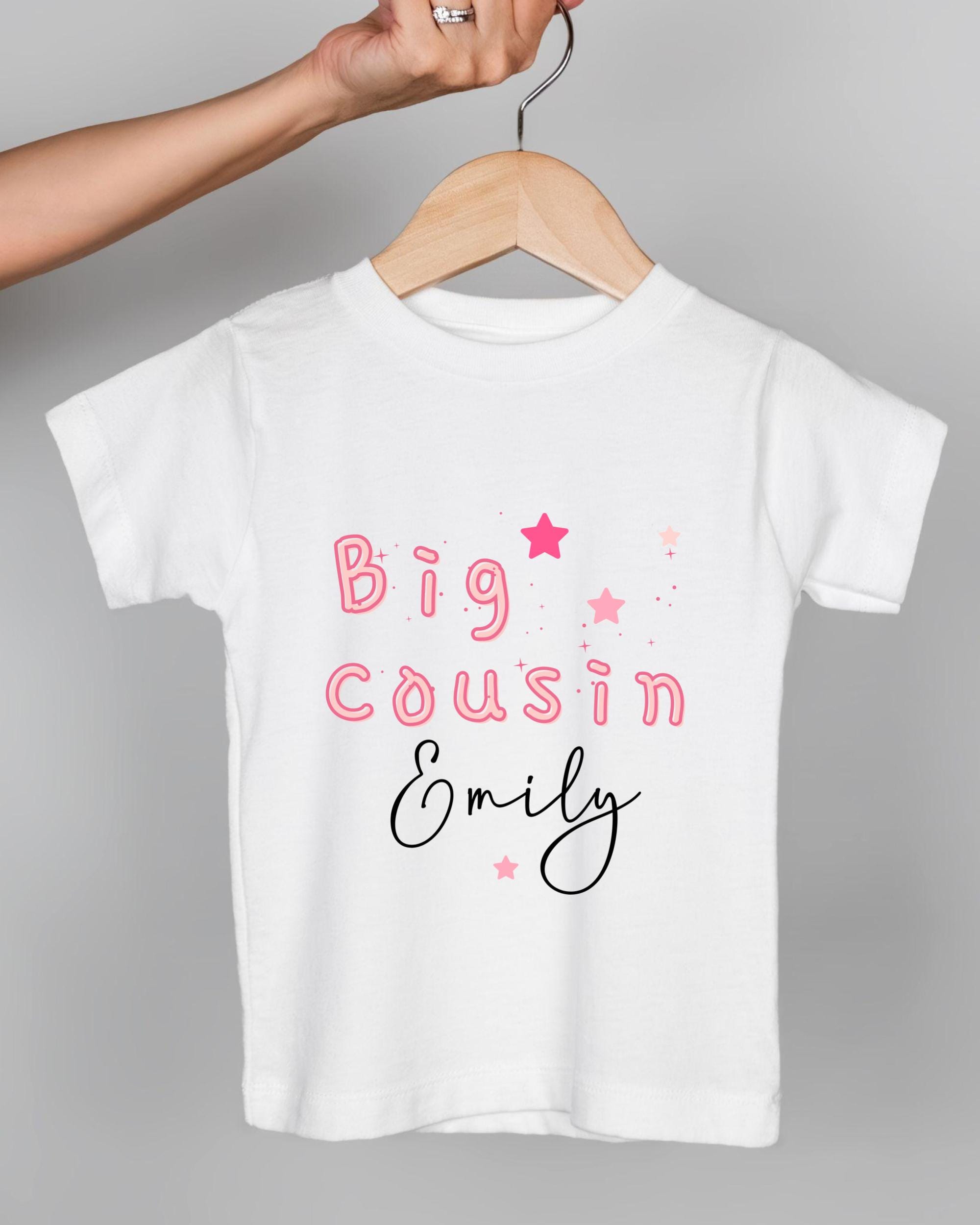 A white t-shirt with pink text and stars printed on it, being held by a person's hand.