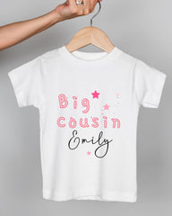 A white t-shirt with pink text and stars printed on it, being held by a person's hand.