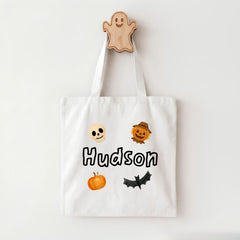 A white tote bag with a name printed on it, featuring a ghost, pumpkin, skeleton, scarecrow, and bat.