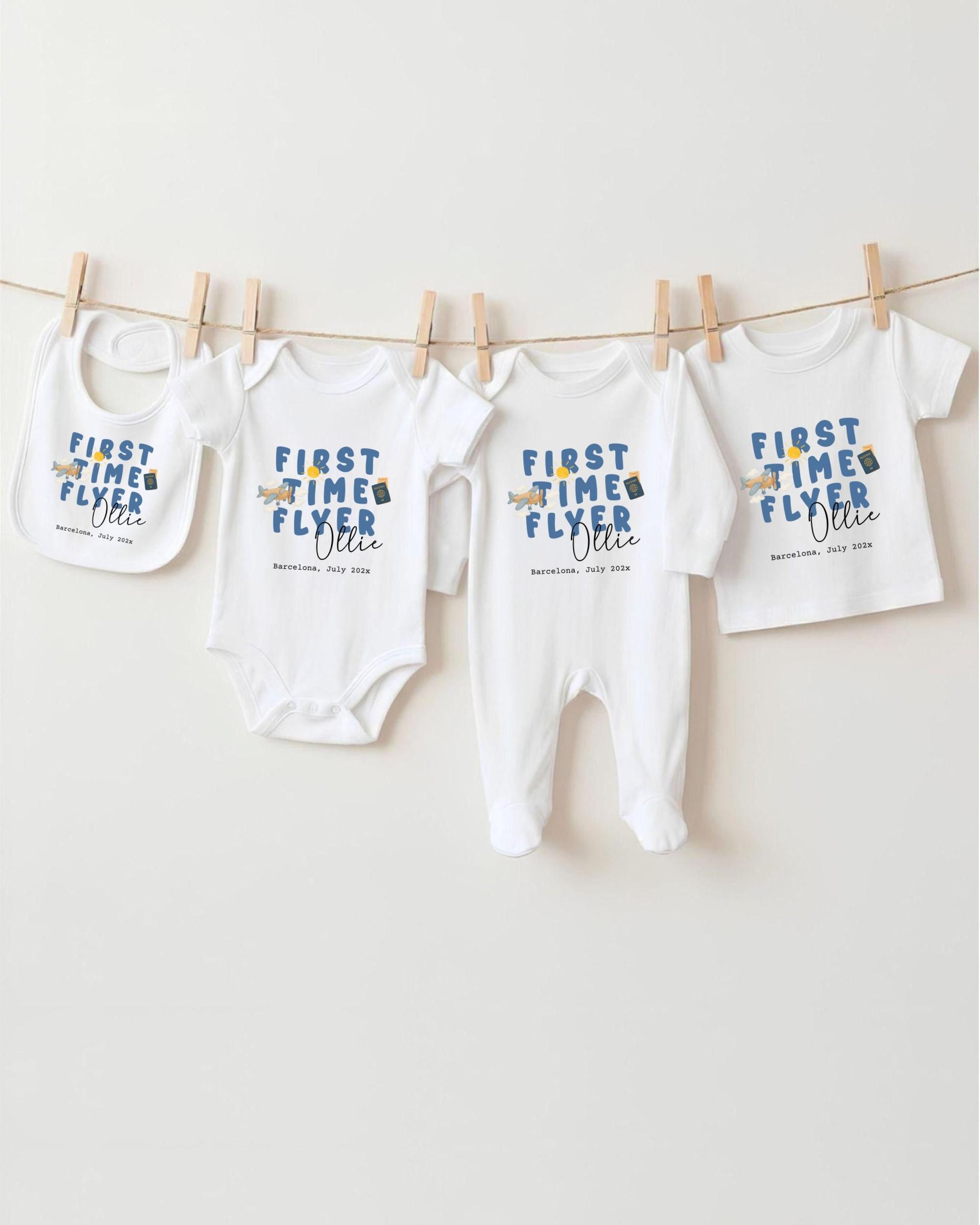 A row of four white baby clothes, including onesies and pajamas, hanging on a clothesline.
