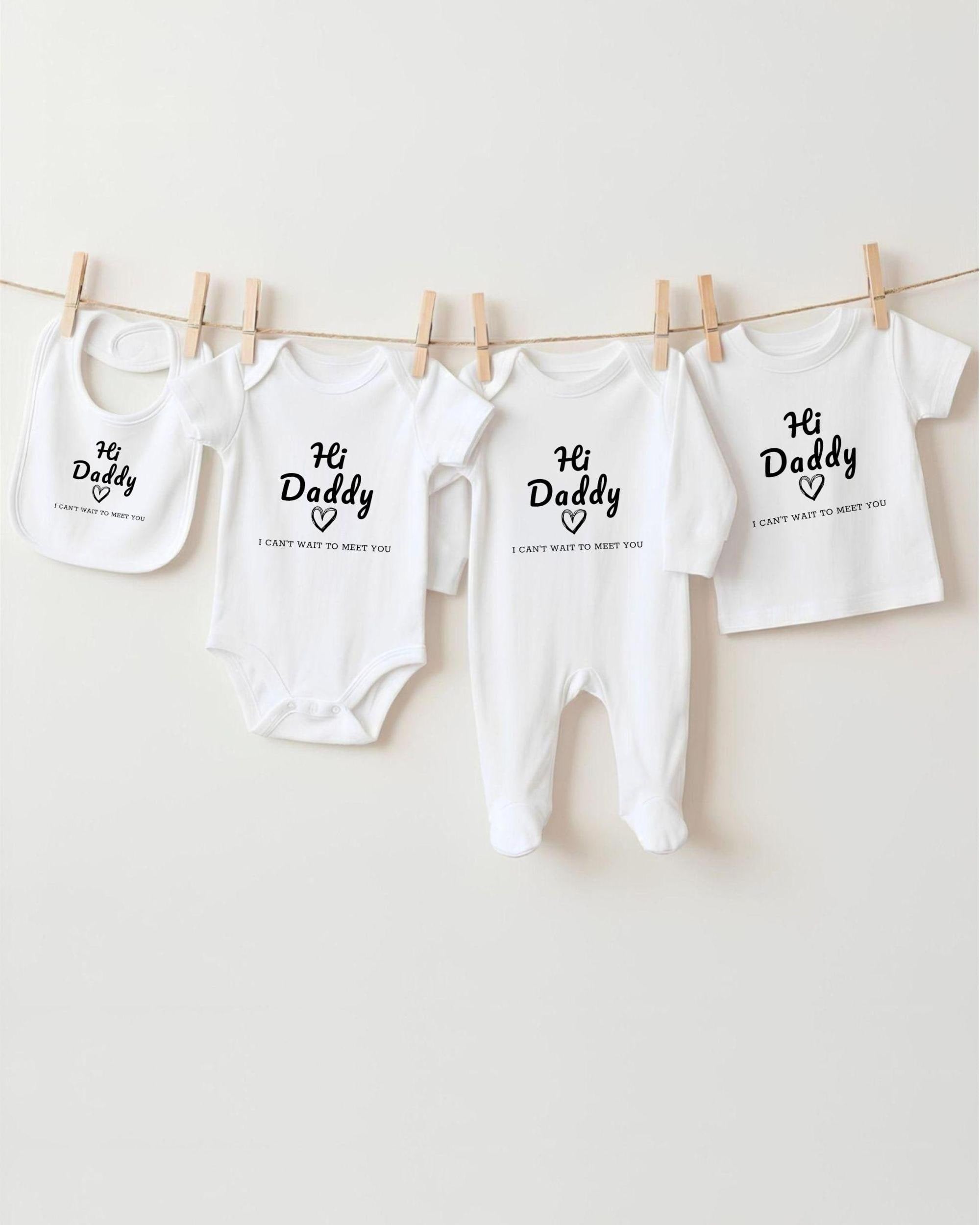 a collection of four white baby clothes, each with a unique message printed on it. The clothes include a bib, a onesie, a pair of pants, and a shirt. The messages on the clothes read "Hi Daddy" and "I can't wait to meet you".