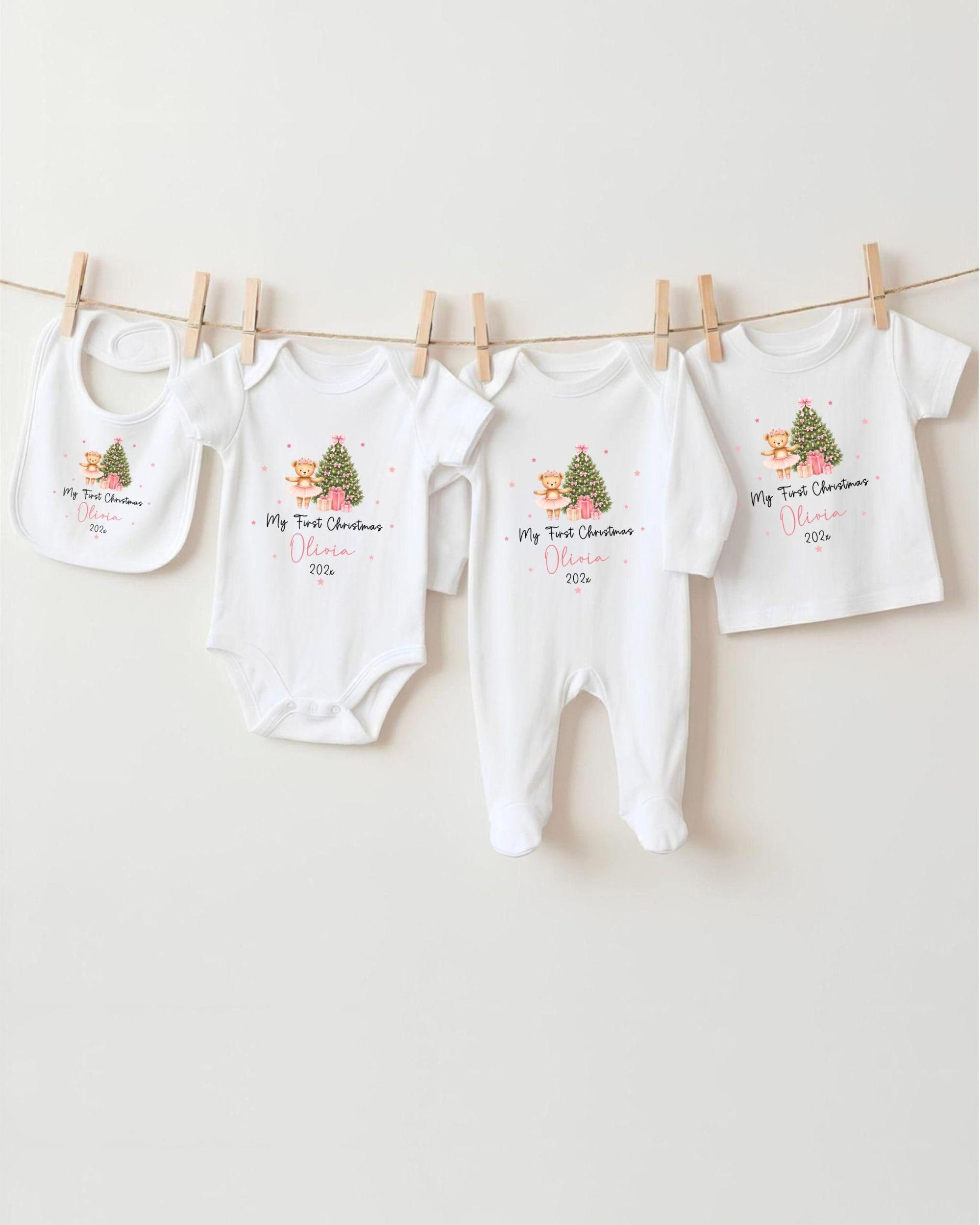 A row of white baby clothes with Christmas-themed designs hanging on a clothesline.