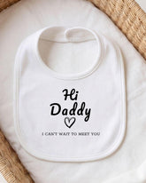 A white bib with the text "Hi Daddy I can't wait to meet you" printed on it, placed on a white cloth.