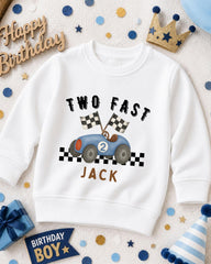 A white sweatshirt with a racing car design and the text "TWO FAST JACK" printed on it, surrounded by birthday decorations and a crown.