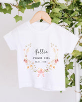 A white t-shirt with a floral design and text printed on it, hanging on a wooden hanger.