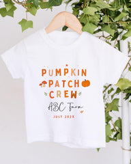 A white t-shirt with text and illustrations related to a pumpkin patch crew, hanging on a wooden hanger.