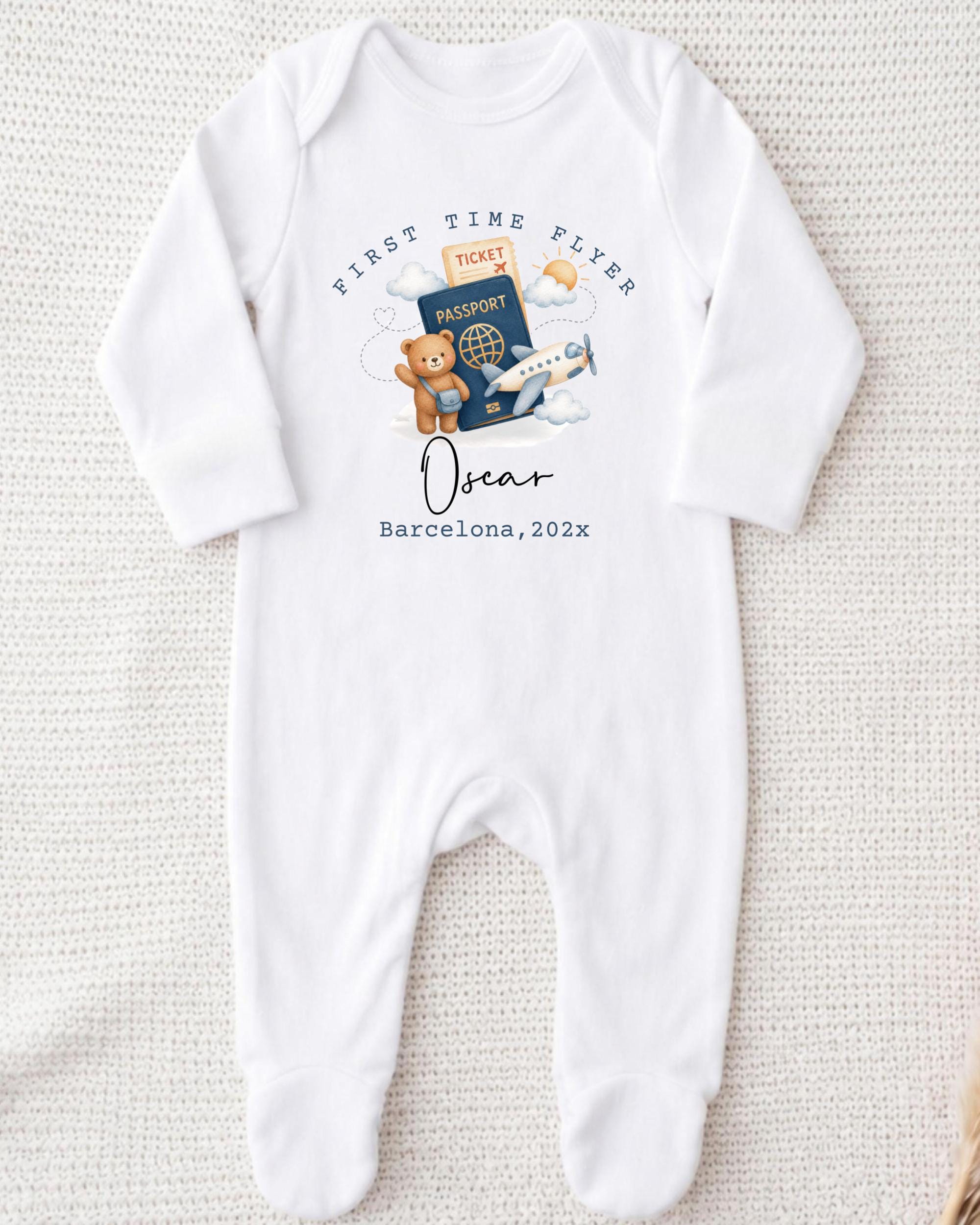 A white onesie with a graphic design depicting a teddy bear, a passport, and an airplane, along with the text "First Time Flyer Oscar Barcelona, 2023".