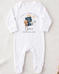 A white onesie with a graphic design depicting a teddy bear, a passport, and an airplane, along with the text "First Time Flyer Oscar Barcelona, 2023".