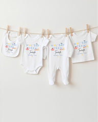A row of white baby clothes, including onesies and bibs, hanging on a clothesline.