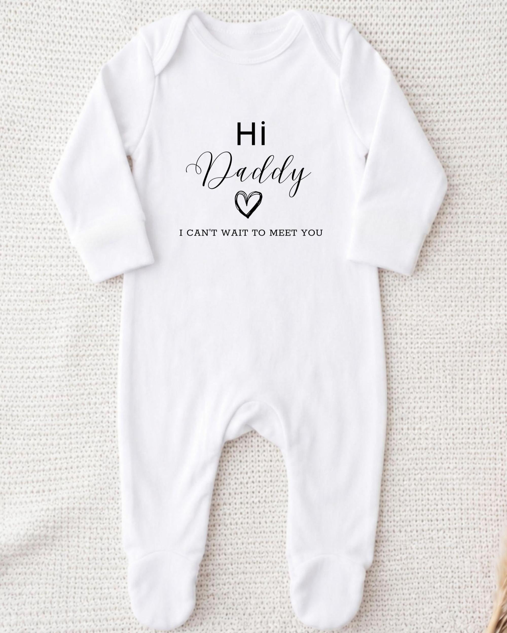 A white onesie with the text "Hi Daddy I can't wait to meet you" printed on it.