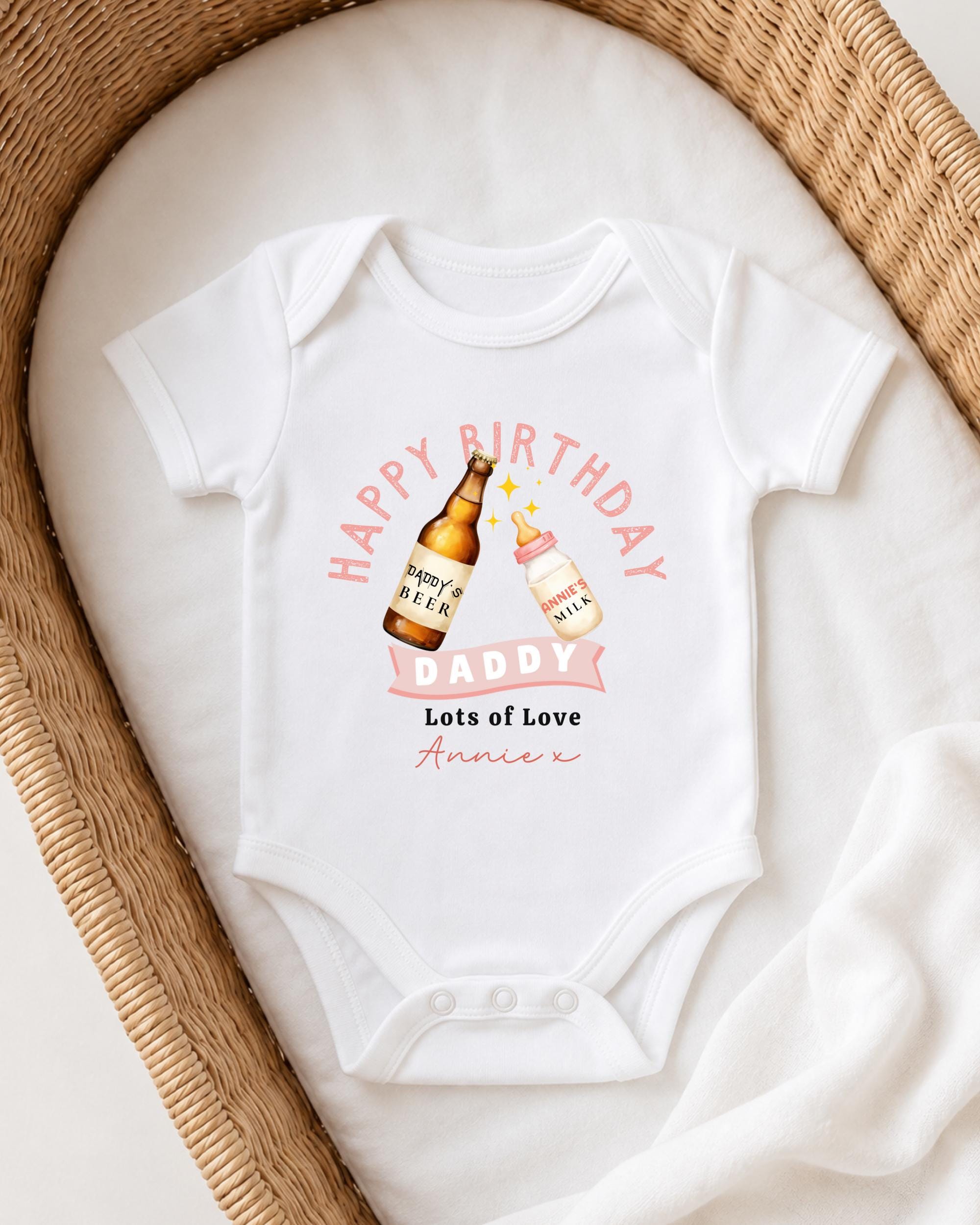 A white onesie with a graphic design on it, featuring a bottle of beer and a bottle of milk, along with the text "Happy Birthday Daddy Lots of Love Annie" printed on it.