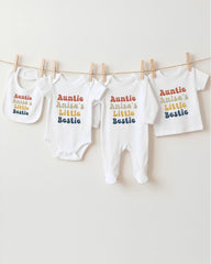 A row of white baby clothes with the text "Auntie Anisa's Little Bestie" printed on them, hanging on a clothesline.