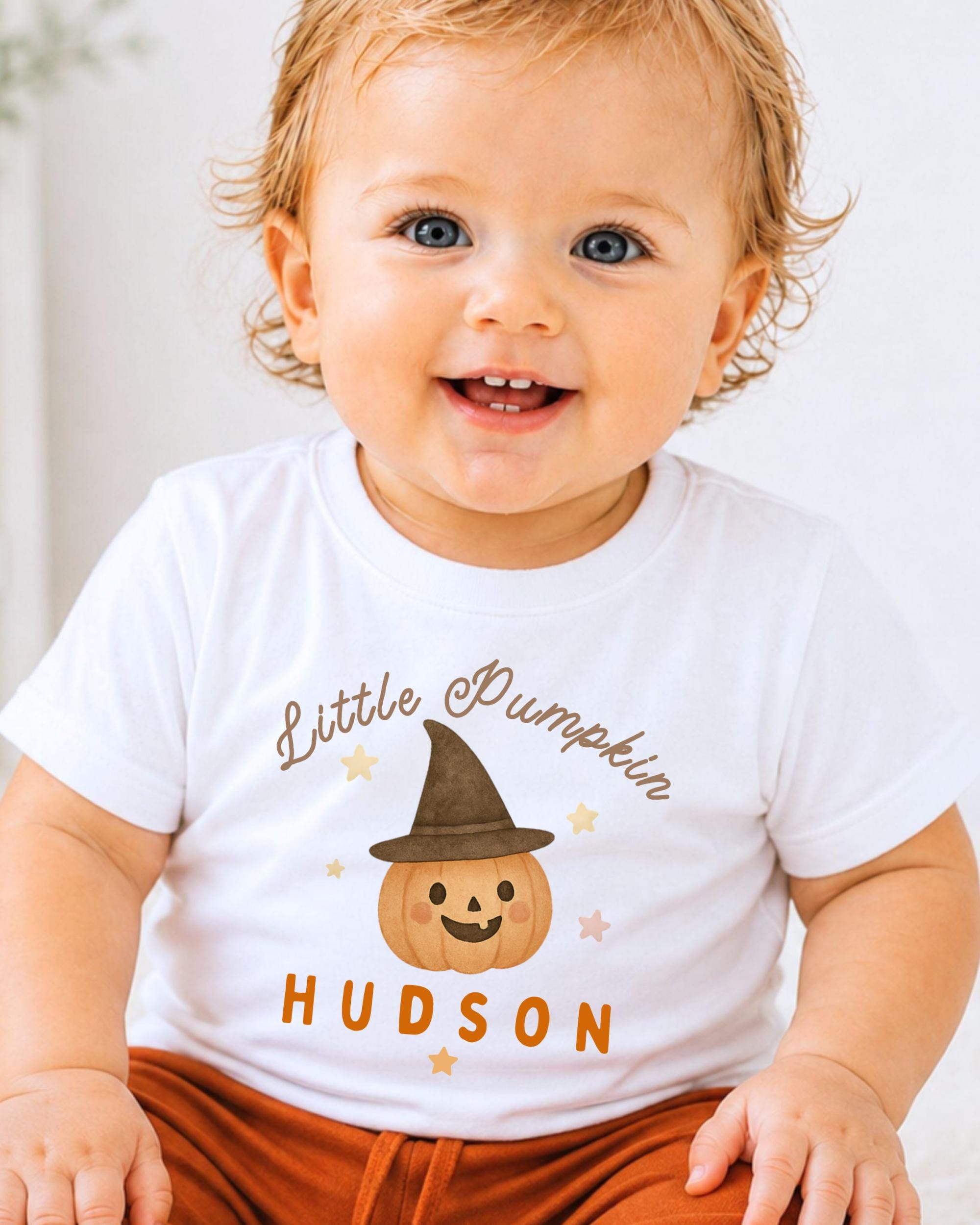 A smiling baby wearing a white t-shirt with a pumpkin graphic and the text "Little Pumpkin" and "Hudson" printed on it.