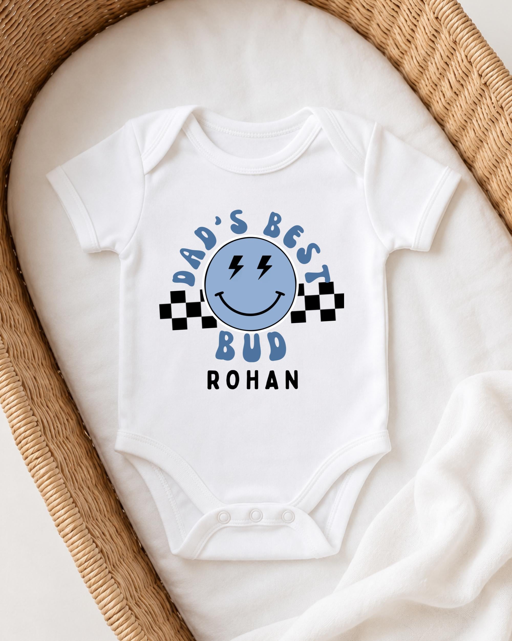 A white onesie with a blue smiley face and text printed on it, placed in a woven basket.