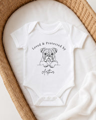 A white baby onesie with a black dog illustration and the text "Loved & Protected by Arthur" printed on it.