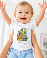 A smiling baby wearing a white t-shirt with a jungle-themed graphic and the name "Jackson" printed on it, being held up by someone's arms.