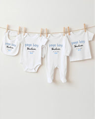 A row of four white baby clothes, each with a personalized name printed on it, hanging on a clothesline.