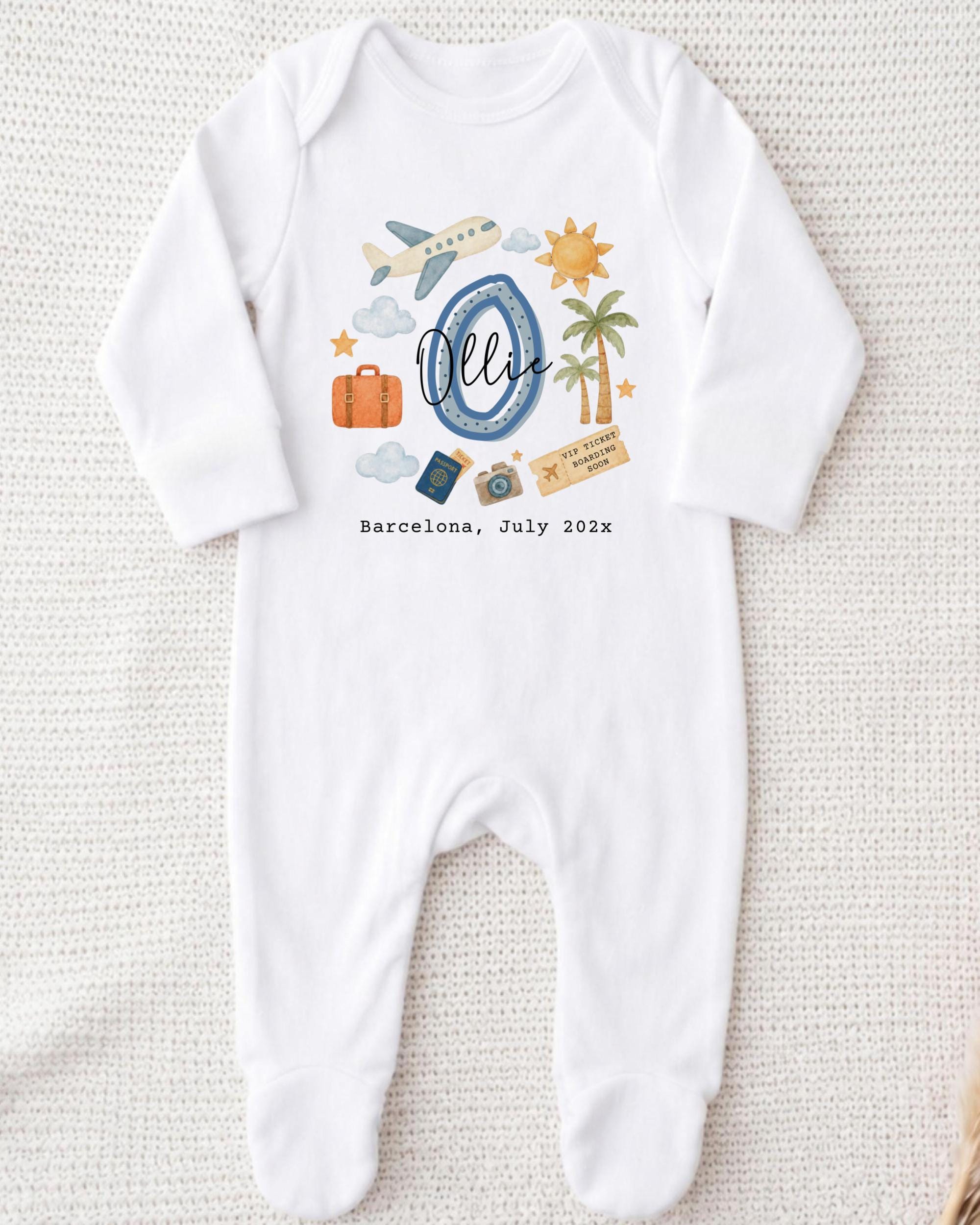 A white onesie with a graphic design depicting various travel-related items such as a suitcase, airplane, palm tree, and a sun. The text "Barcelona, July 2020" is also printed on the onesie.