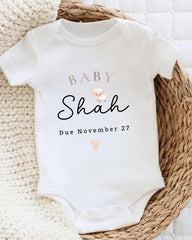 A white baby onesie with text and a small animal printed on it, placed on a woven basket.