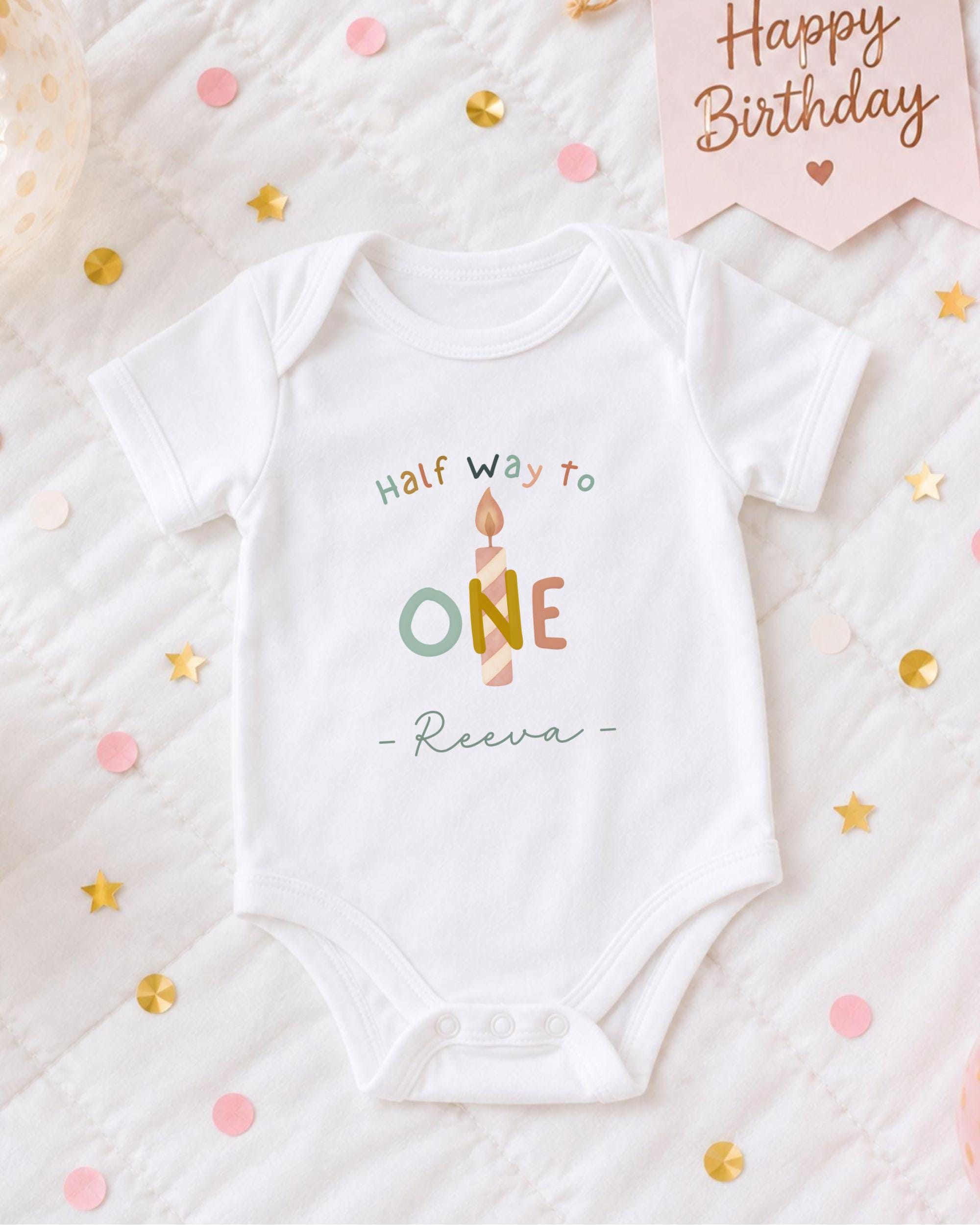A white onesie with the text "Half way to one" printed on it, surrounded by confetti and a birthday card.