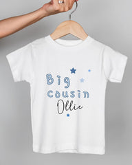 A white t-shirt with the text "Big Cousin Ollie" printed on it, along with blue stars.