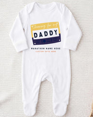 A white onesie with a graphic design on it, featuring a yellow and blue rectangle with the text "Cheering for my DADDY" and "MARCHON NAME HERE" below it.