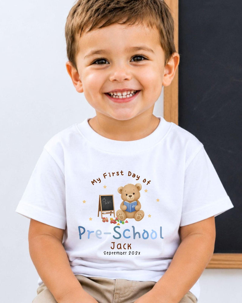 A young boy wearing a white t-shirt with a teddy bear and a chalkboard, smiling at the camera.