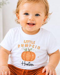 A smiling baby wearing a white t-shirt with a pumpkin graphic and text that says "Little Pumpkin" and "Huxton".