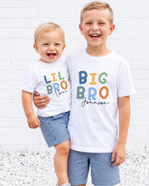 Two young boys wearing matching white t-shirts with the text "Lil Bro Johnson" printed on them, smiling and posing together.