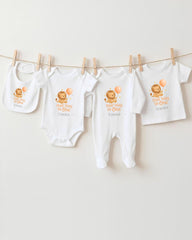 A collection of baby clothes, including onesies and bibs, hanging on a clothesline.
