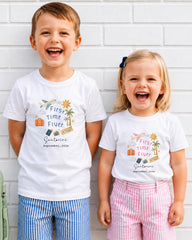 Two children, a boy and a girl, are standing next to each other and smiling, wearing matching white t-shirts with text and illustrations.