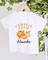 A white t-shirt with a graphic design featuring three pumpkins and the text "Pumpkin Crew Alexander" printed on it.