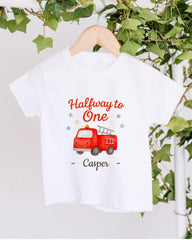 A white t-shirt with a red fire truck graphic and the text "Halfway to One - Casper" printed on it, hanging on a wooden hanger.