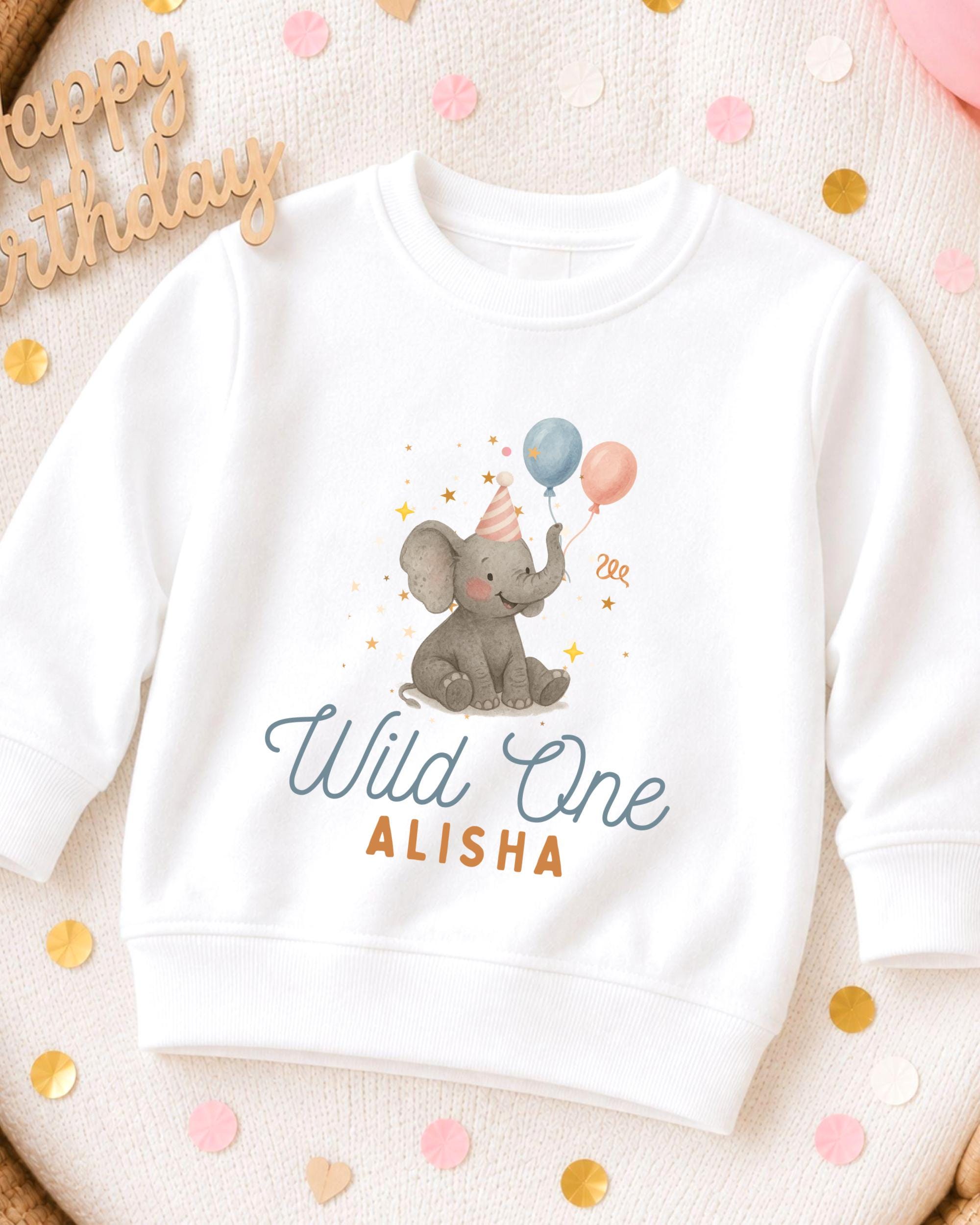 A white sweatshirt with a graphic of an elephant wearing a party hat and holding balloons, along with the text "Wild One ALISHA".