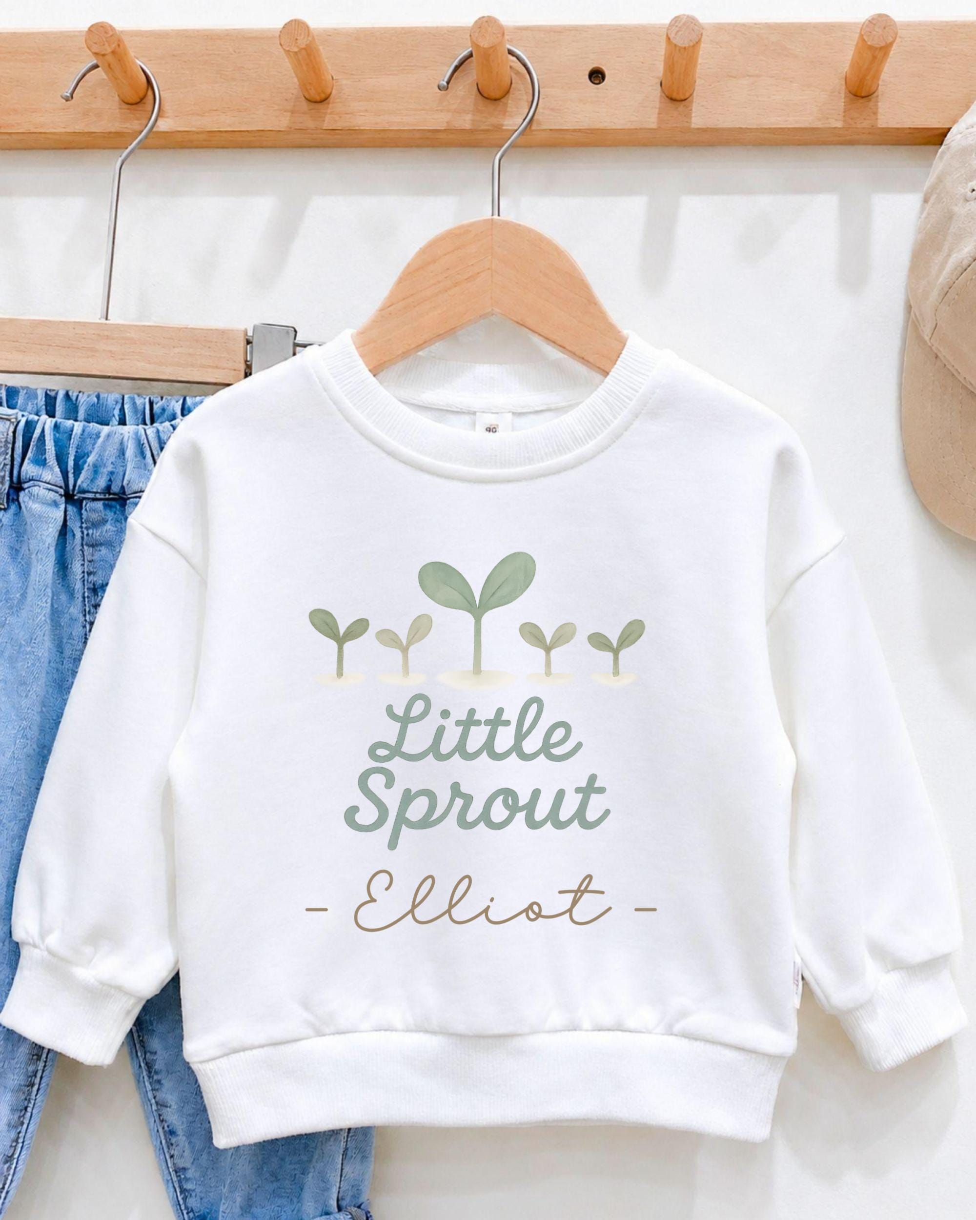A white sweatshirt with a graphic design and text printed on it, hanging on a wooden hanger.